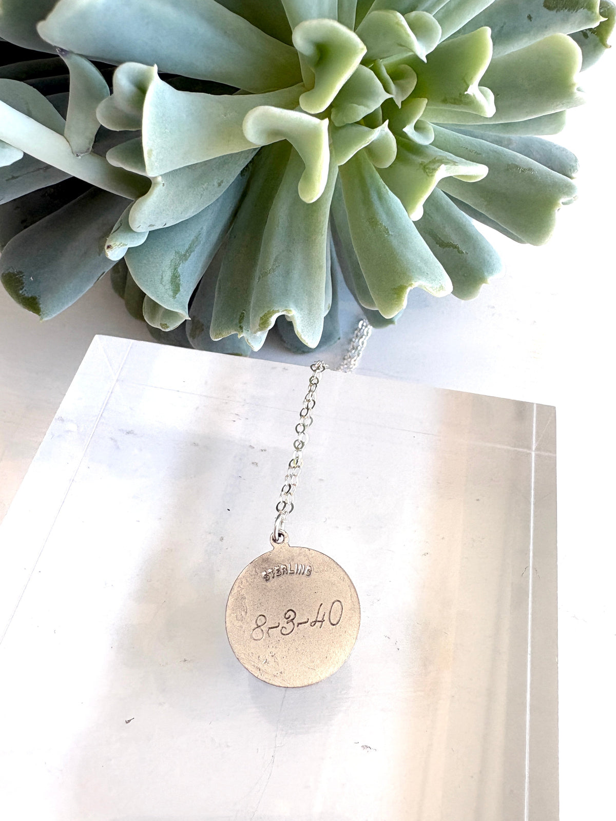 A silver necklace with a round engraved pendant